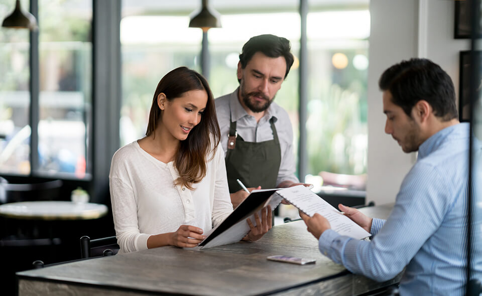 A man and a woman look over menus as a waiter stands nearby